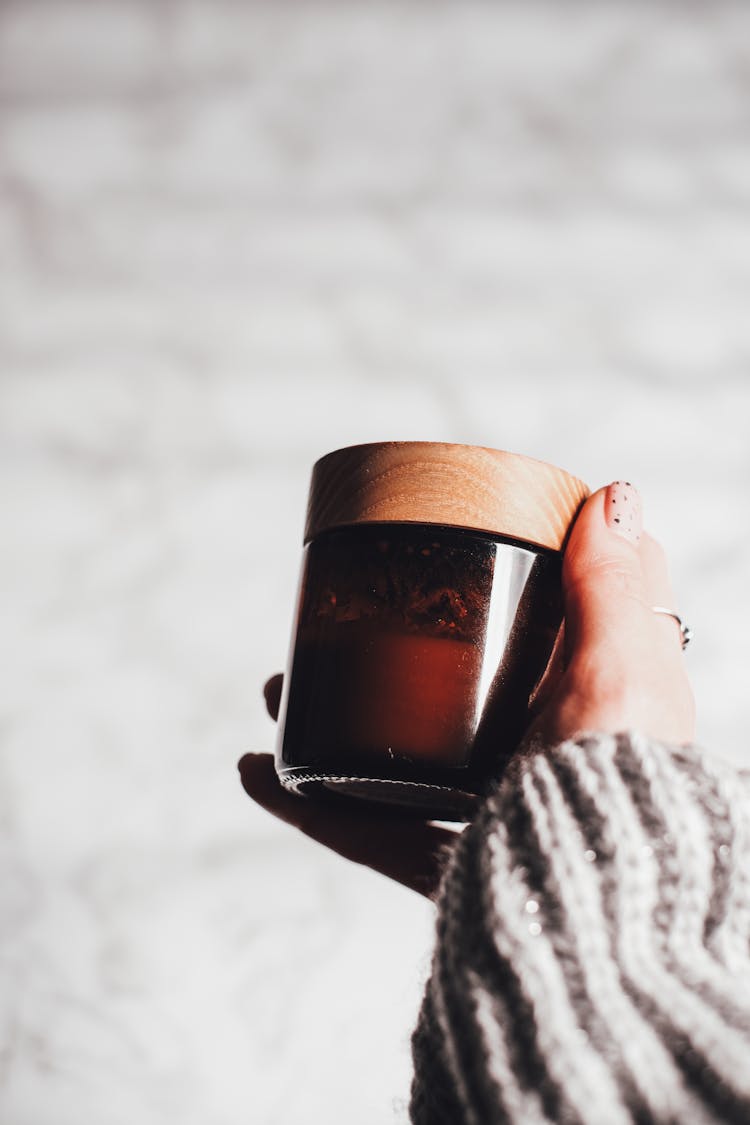 Hand Holding A Brown Glass Jar With Wooden Lid 