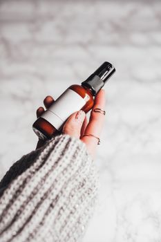 A stylish close-up of a woman holding a skincare product in a glass bottle with a marble background.