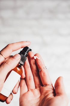 Close-up image of a hand applying cream from a bottle, demonstrating cosmetic product use.