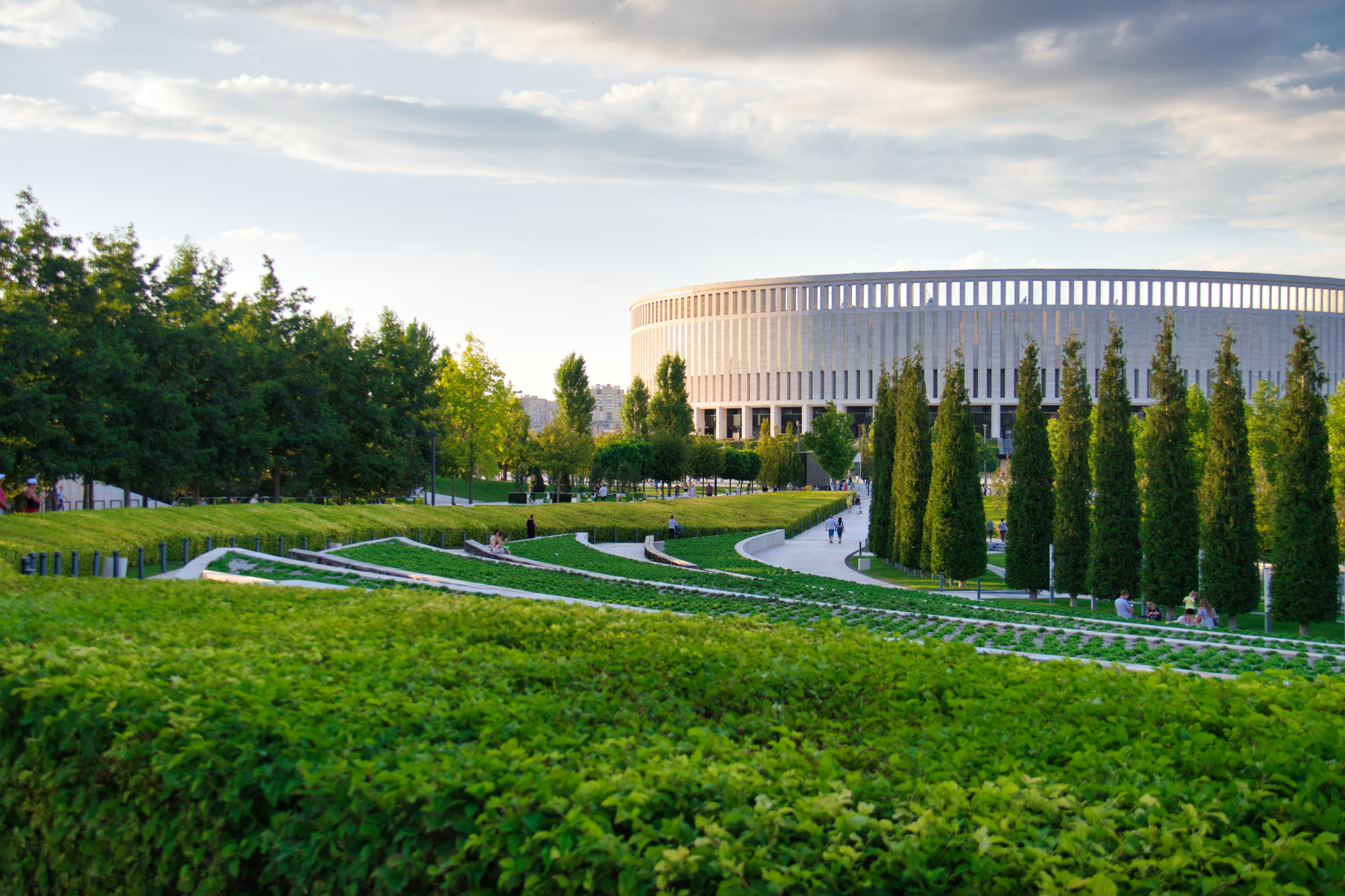Imagem de um espaço verde bem cuidado na frente de um estádio moderno, ideal para ilustrar temas de planejamento urbano e sustentabilidade em espaços públicos.