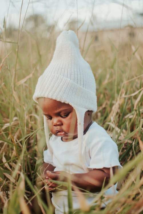 Free Cute Baby in White Clothing sitting on Grass Stock Photo