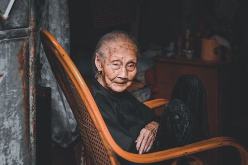 Free Portrait of an elderly woman sitting in a rocking chair indoors with a contemplative look. Stock Photo