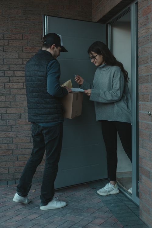 Free A delivery person hands a package to a woman at her home door. Stock Photo