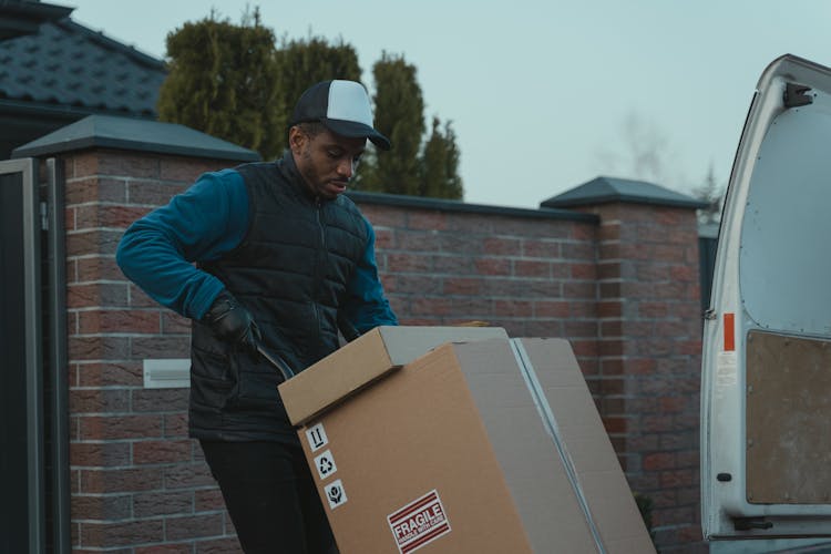 A Man In Black Vest Pushing A Trolley With Carton Boxes