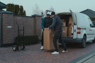 Man in Black Jacket and Blue Denim Jeans Standing Beside Brown Cardboard Box