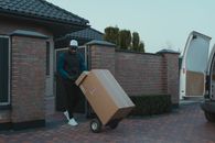 Man in Blue Jacket and Blue Denim Jeans Standing Beside Brown Cardboard Box