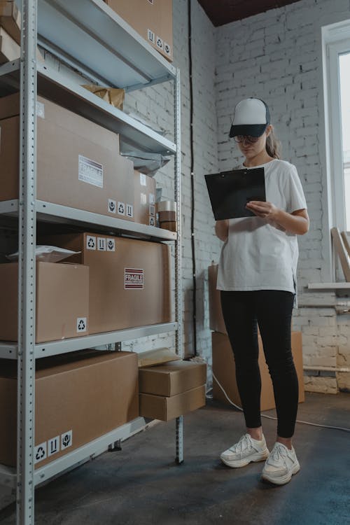 A Woman in White Shirt Standing Near the Shelves with Carton Boxes