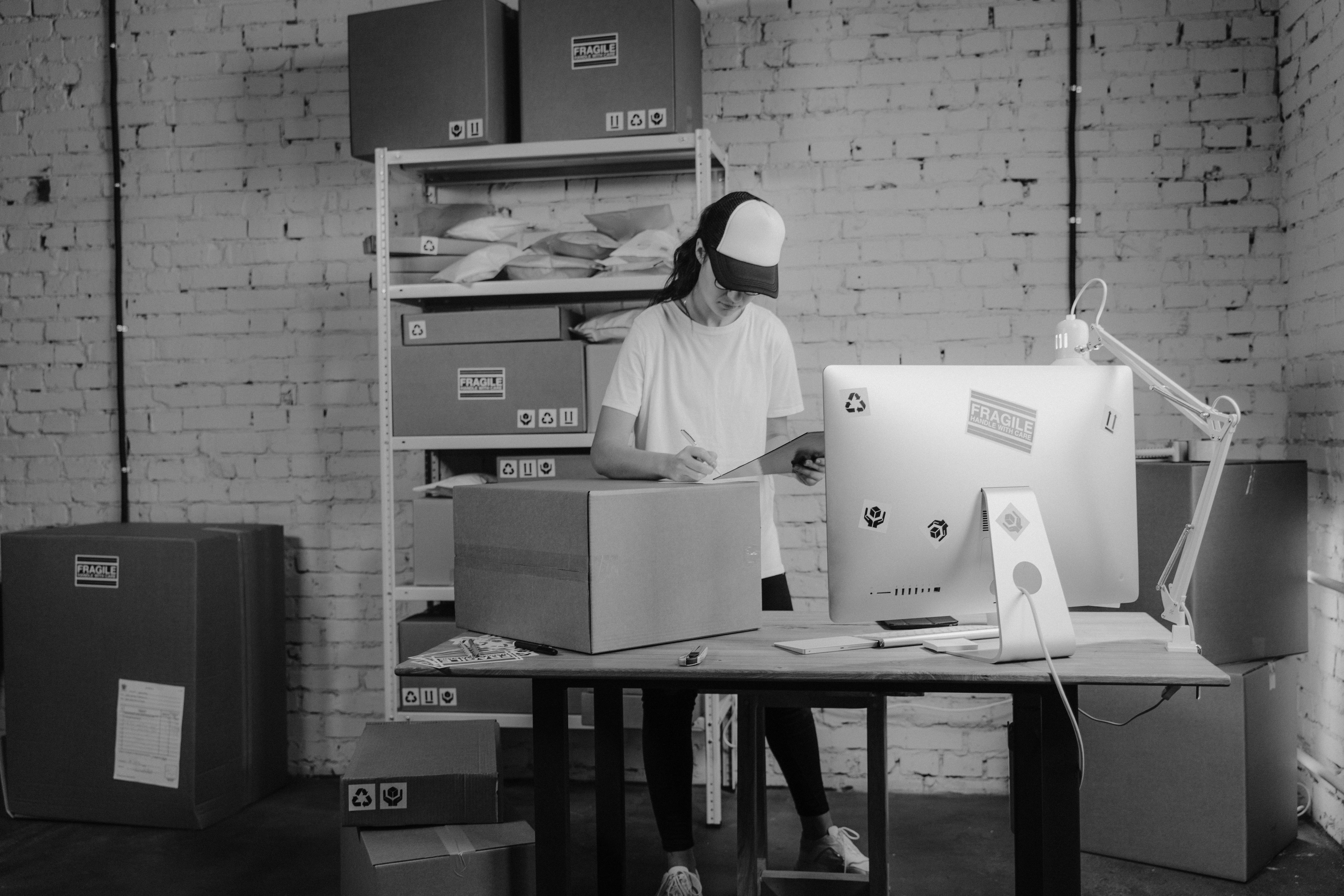 woman writing down on a carton box while looking at a clipboard