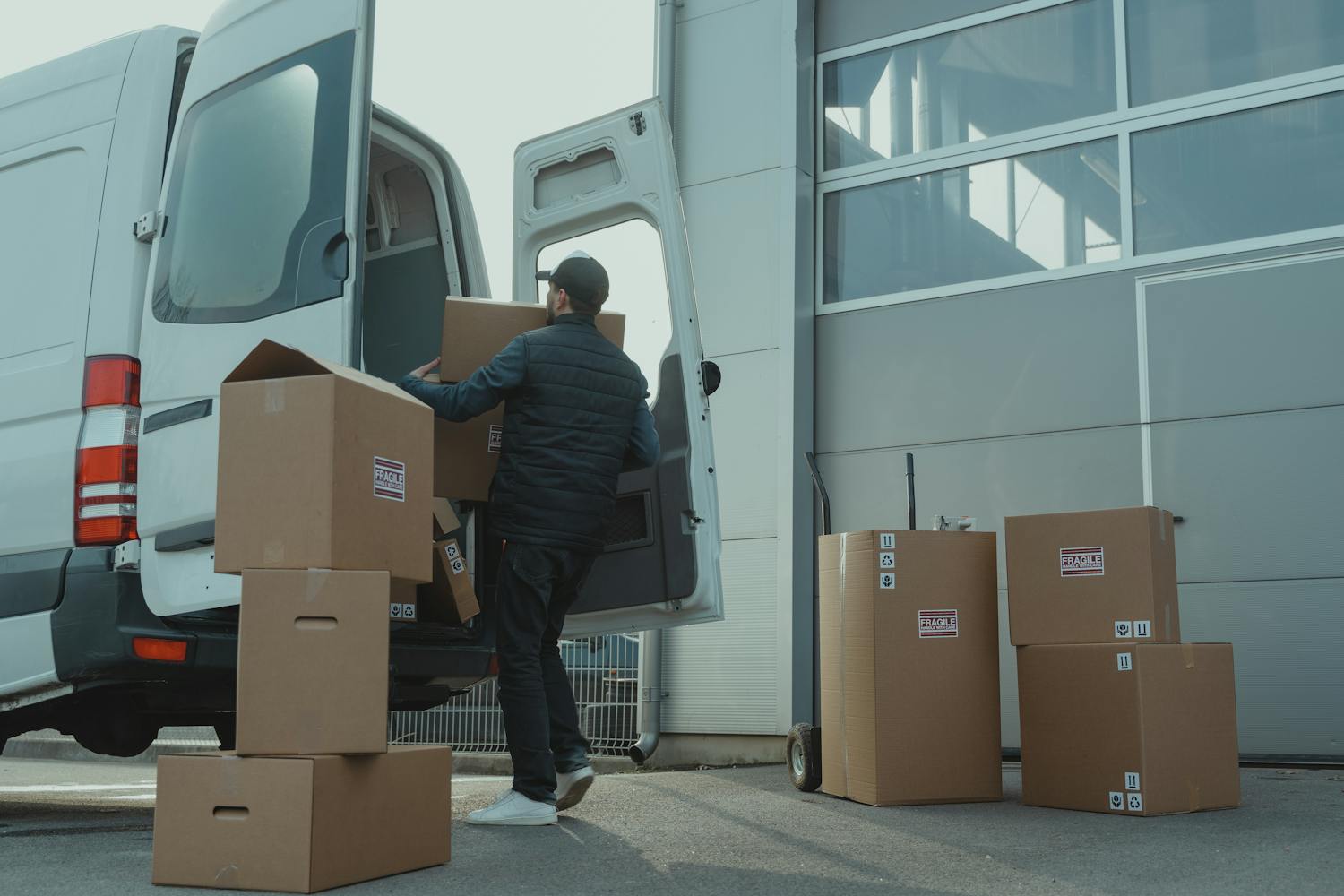 A delivery man unloading cardboard boxes from a van at a warehouse