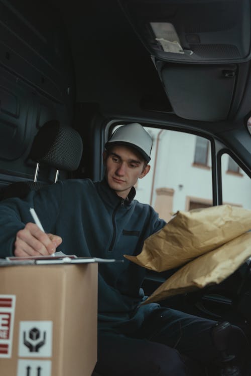 Delivery Man writing on a Paper on Top of a Cardboard Box 