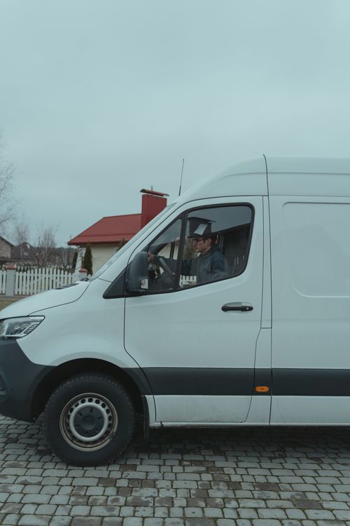 Free Driver in a white van parked on a suburban cobblestone street. Stock Photo