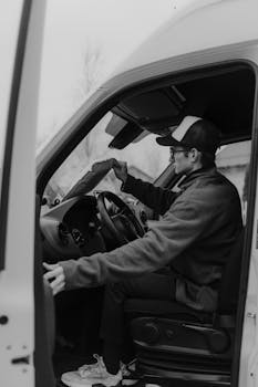 Man in casual attire driving a delivery van, captured in black and white.