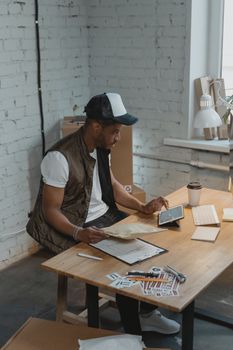 Man in casual attire checking orders on a tablet in a modern office setup, surrounded by packages.