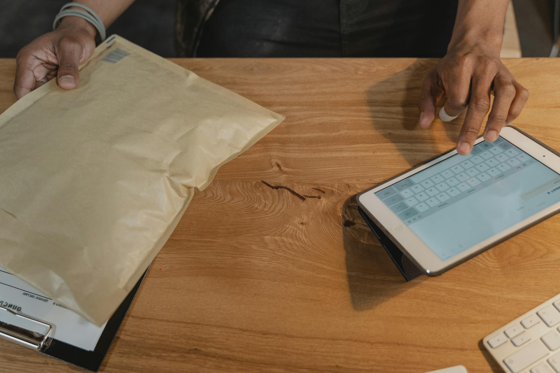 Person managing logistics on a tablet with a parcel on a wooden table.