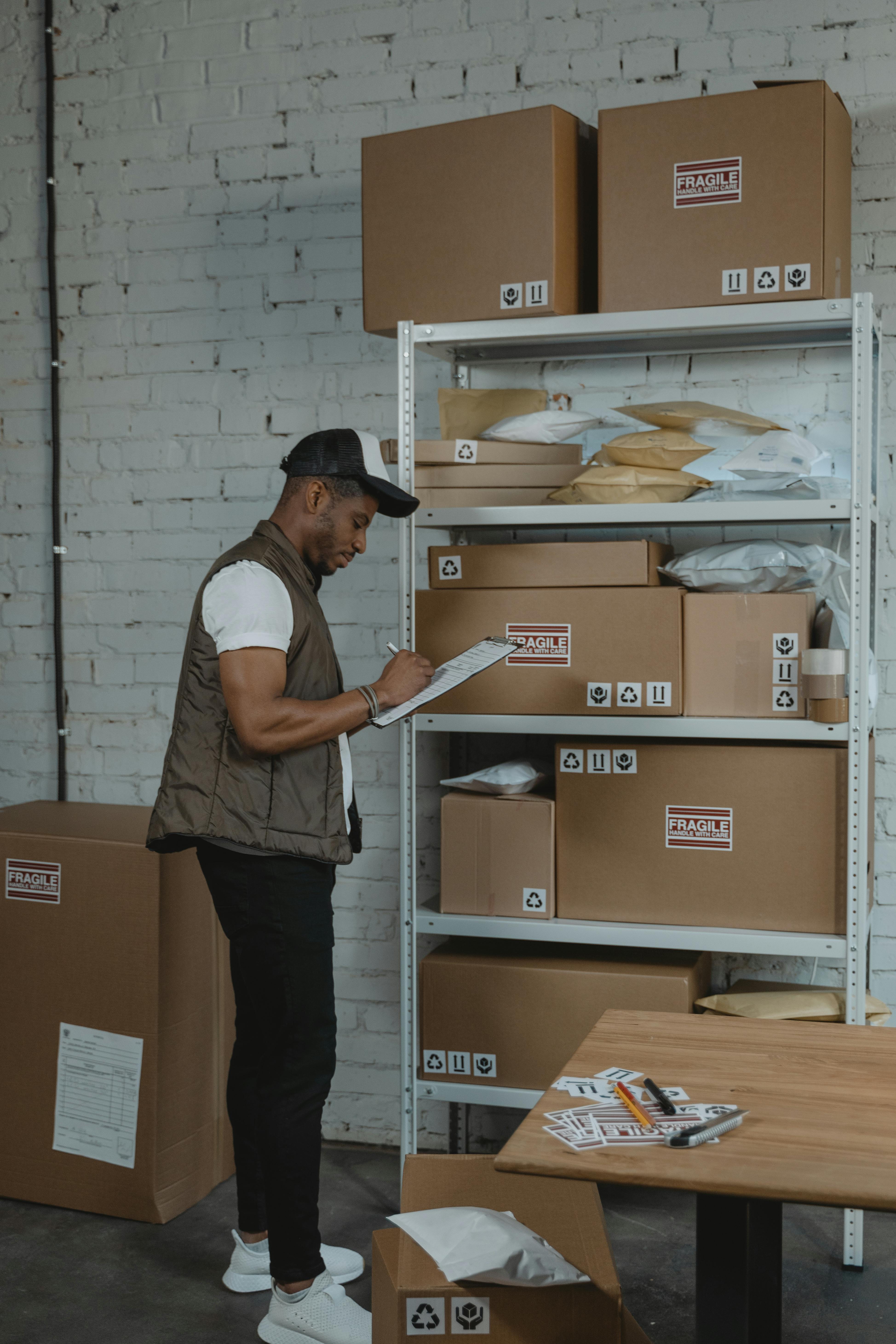 business man writing on a paper while standing beside a shelf of boxes