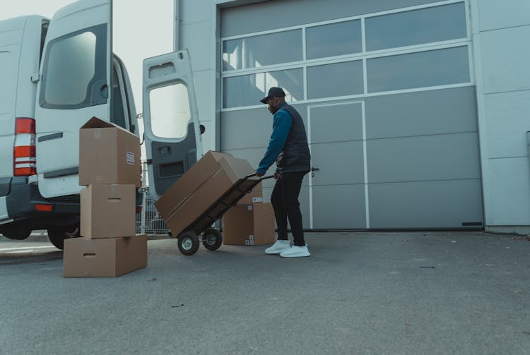 Delivery Man Pulling A Trolley With Carton Boxes