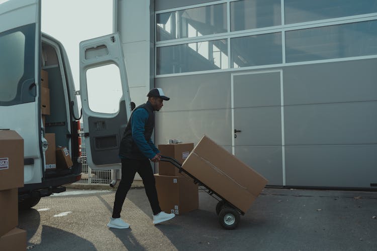 Delivery Man Pushing A Trolley With Carton Boxes