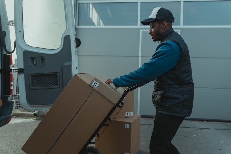 Delivery Man Pushing A Trolley With Carton Boxes