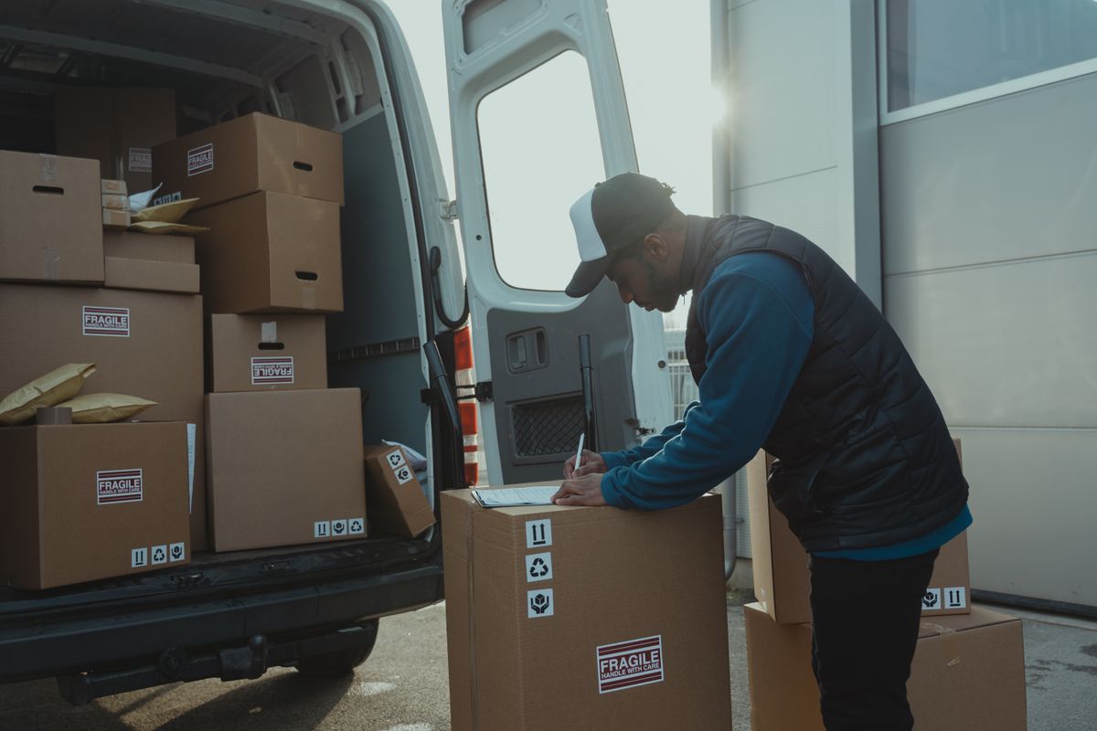 Mover writing on paperwork on top of a carton beside a loaded van, completing the moving inventory and bill of lading