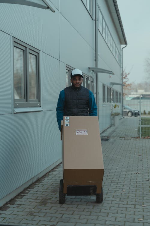 Free Delivery Man pushing a Trolley with Carton Boxes Stock Photo