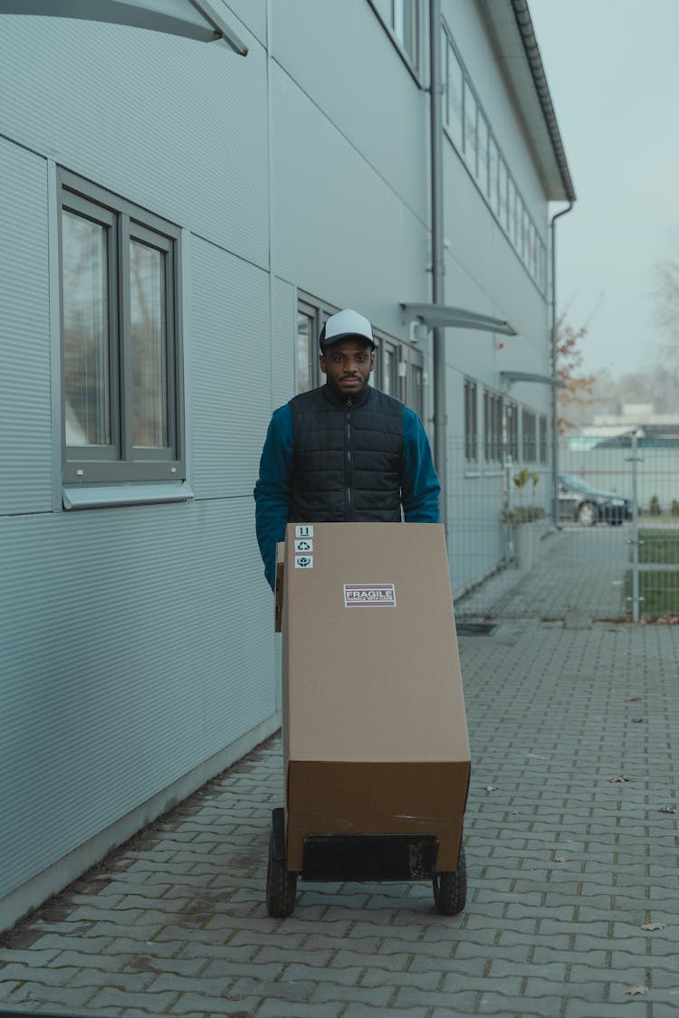 Delivery Man Pushing A Trolley With Carton Boxes