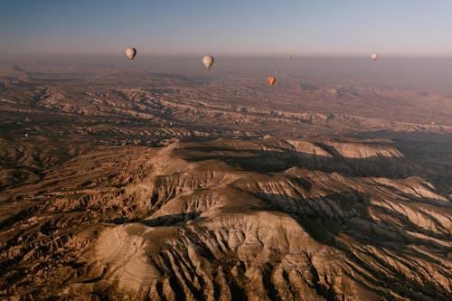 Free Aerial view of hot air balloons soaring over the stunning rock formations of Cappadocia at sunrise. Stock Photo