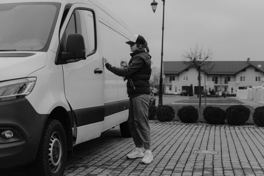 A courier in casual attire delivers a parcel from a van in a suburban street setting.