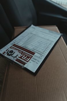 Close-up of a clipboard with documents on a package inside a vehicle, signaling delivery service.