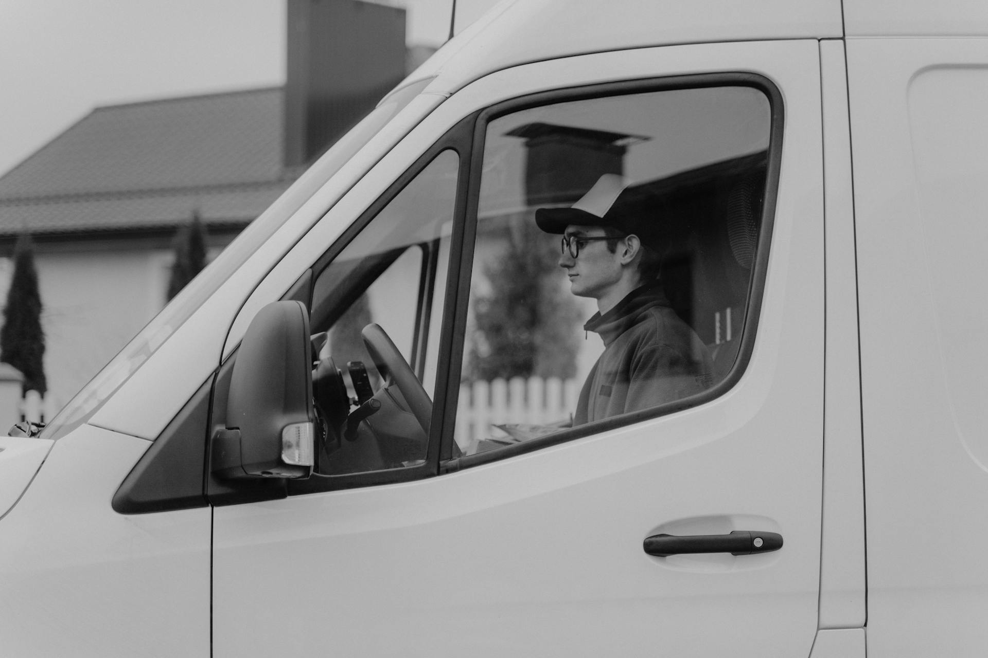 Black and white image of a delivery driver inside a cargo van, showcasing service and transportation.