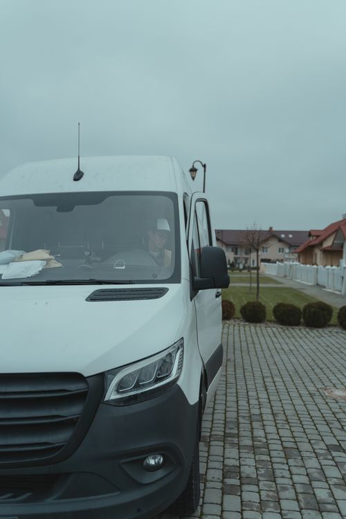 Free White delivery van parked in a suburban area with driver inside on a cloudy day. Stock Photo