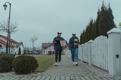 Man in Black Jacket and Blue Denim Jeans Walking on Pathway