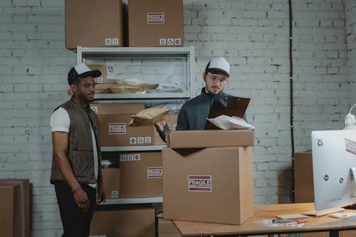 Man in Black Polo Shirt Standing Beside Brown Cardboard Box