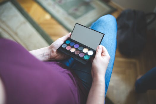 A woman holding an eyeshadow palette, showcasing various makeup colors indoors, captured with Canon EOS 6D.