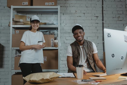 Two warehouse employees in casual attire smiling while working in a courier environment with packages.