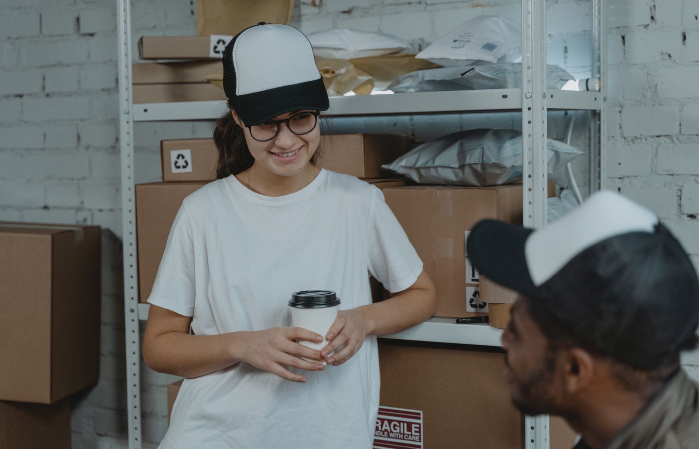 Two employees having a break and chatting in a warehouse, surrounded by packages and boxes.