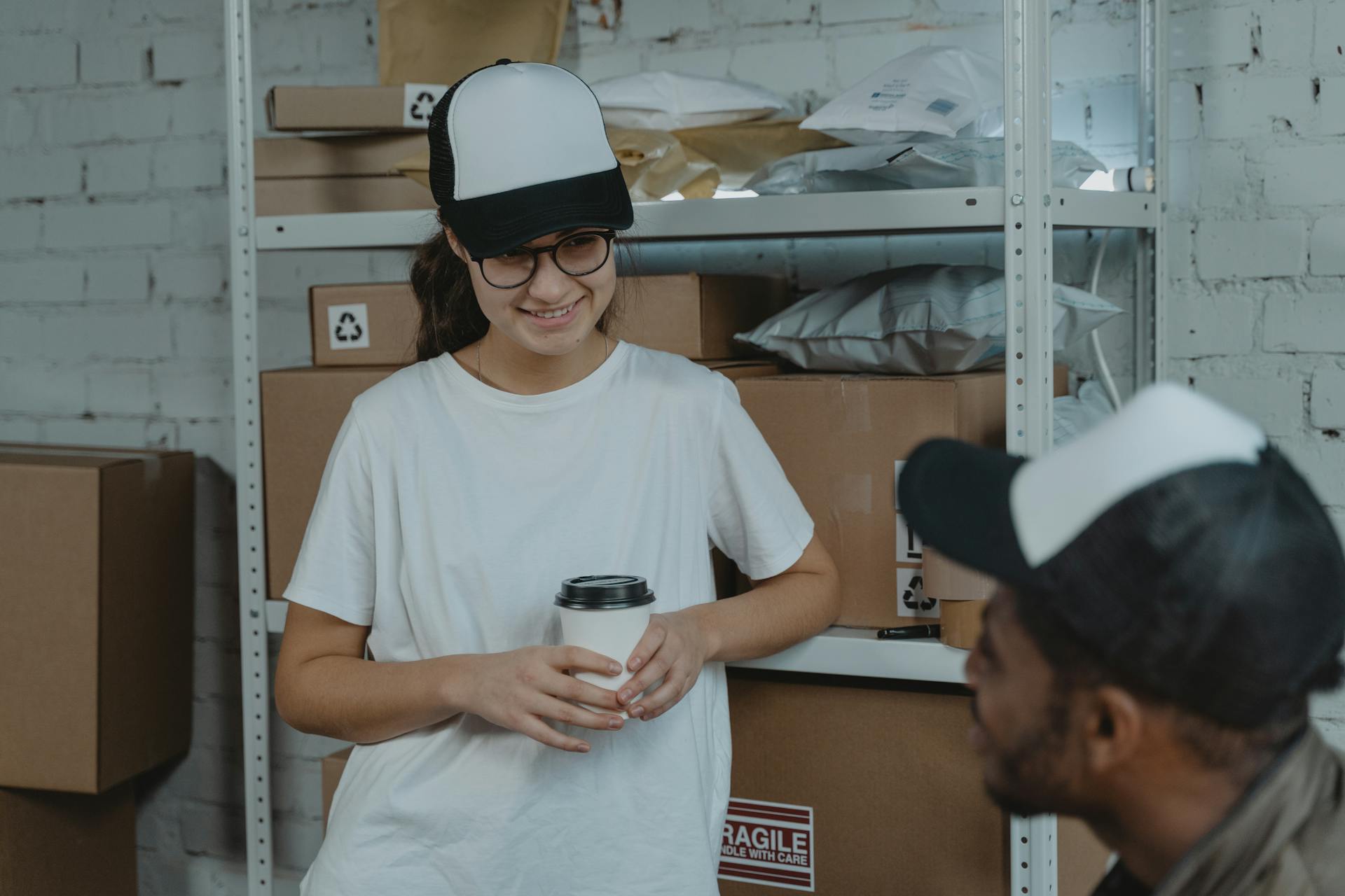 Two employees having a break and chatting in a warehouse, surrounded by packages and boxes.