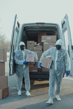 Logistics workers in protective gear unload packages from a delivery van outdoors.