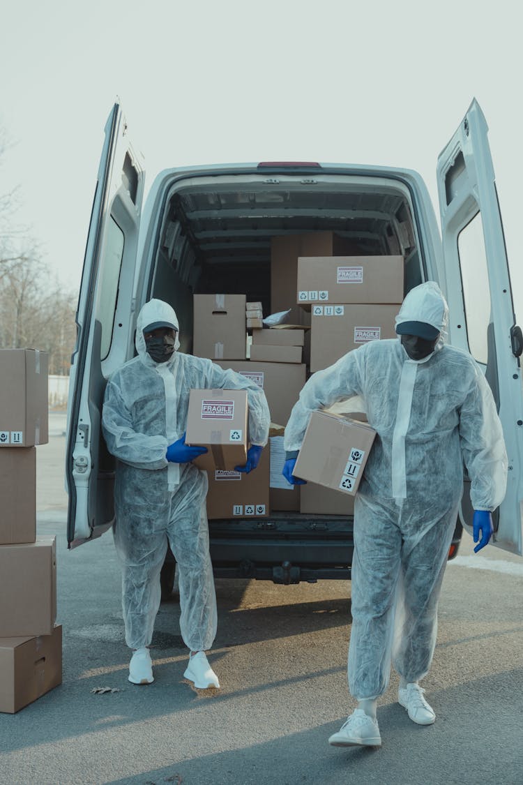 Two Delivery Men In PPE Carrying A Box