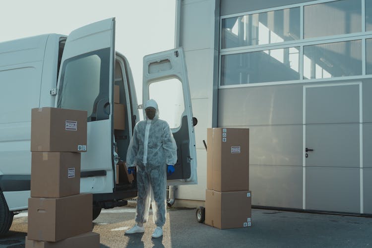 Delivery Man In PPE Standing Beside A Delivery Van 