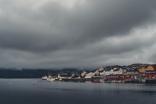 Gjesvær harbor with dark storm clouds above, colorful waterfront houses in Norway.