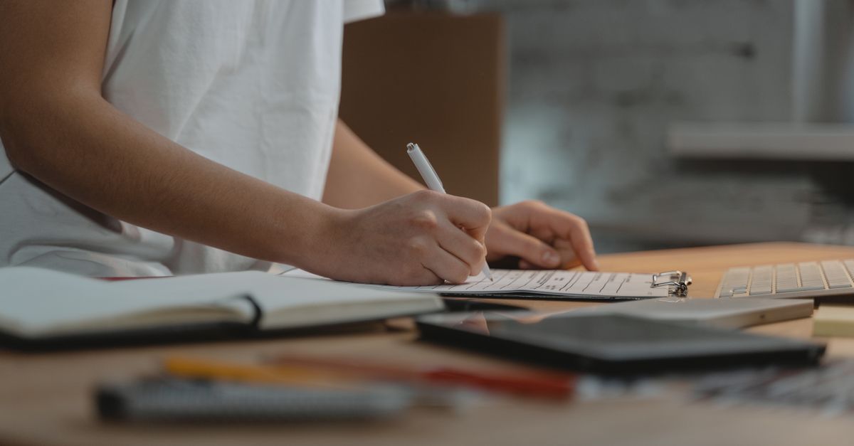 Close-up of individual writing on a clipboard at a desk with office supplies.