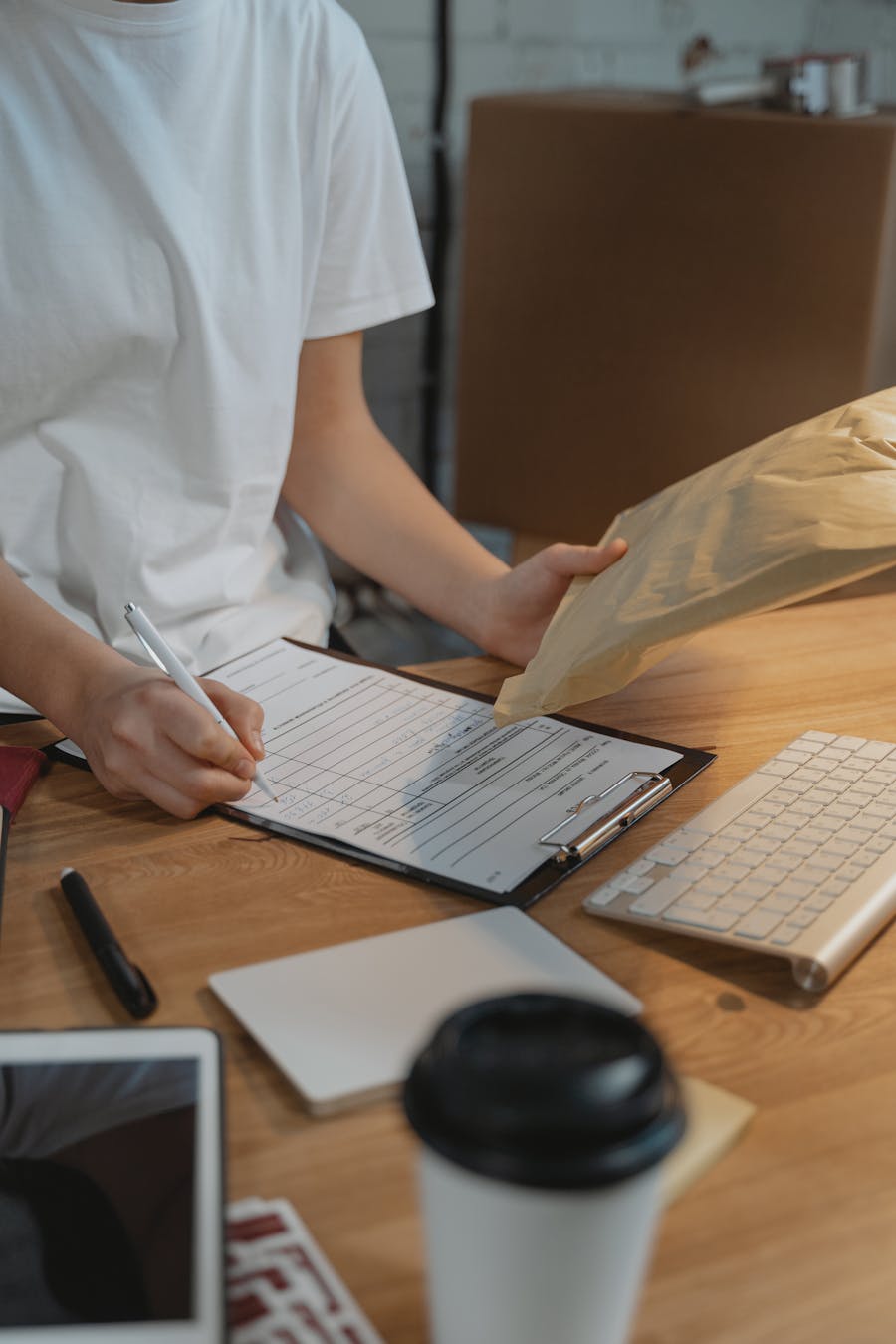 Close-up of a person filling a document on a clipboard with a parcel on a desk.