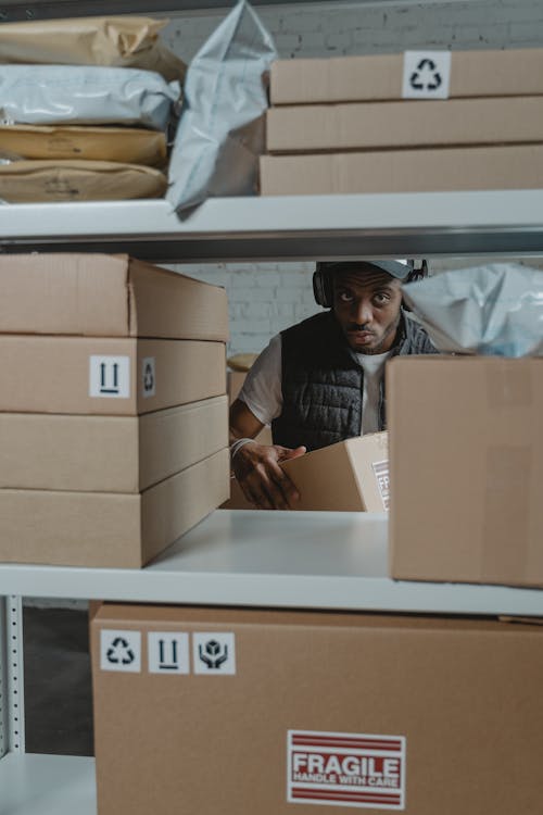 A Man Standing Behind a Shelf With Cardboard Boxes