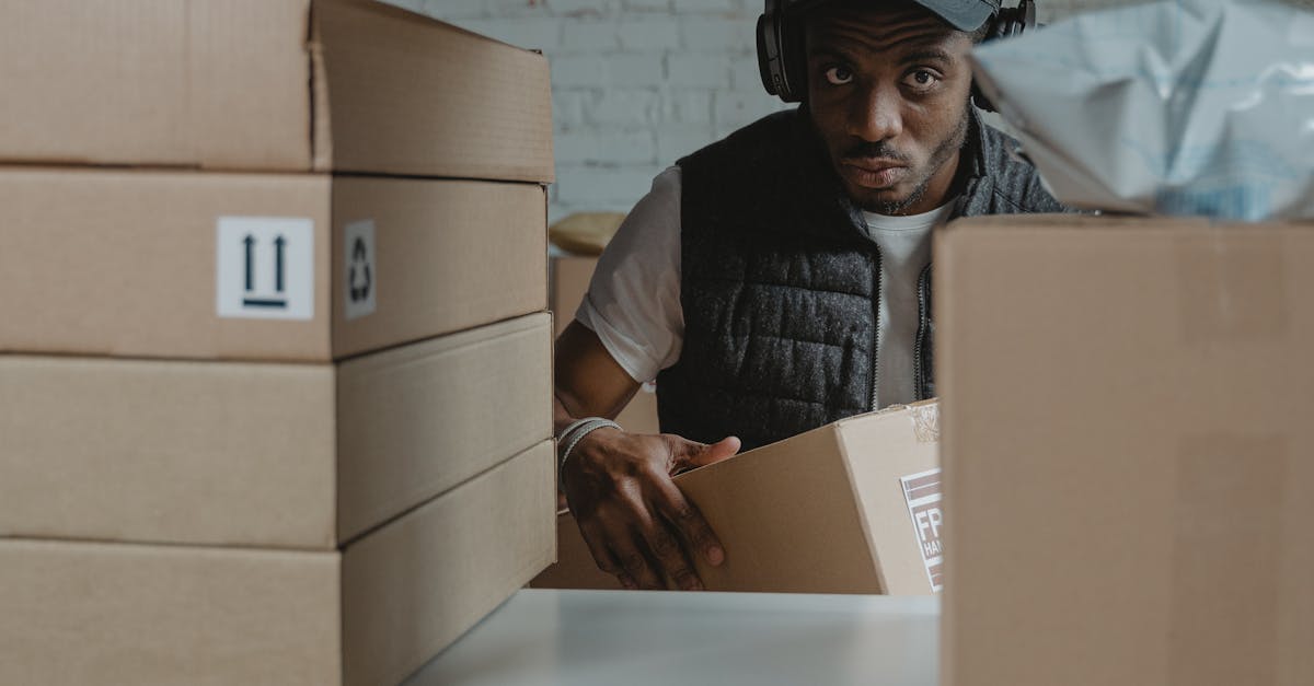 Photo by Tima Miroshnichenko Man organizing packages on shelves in a warehouse setting with cardboard boxes.