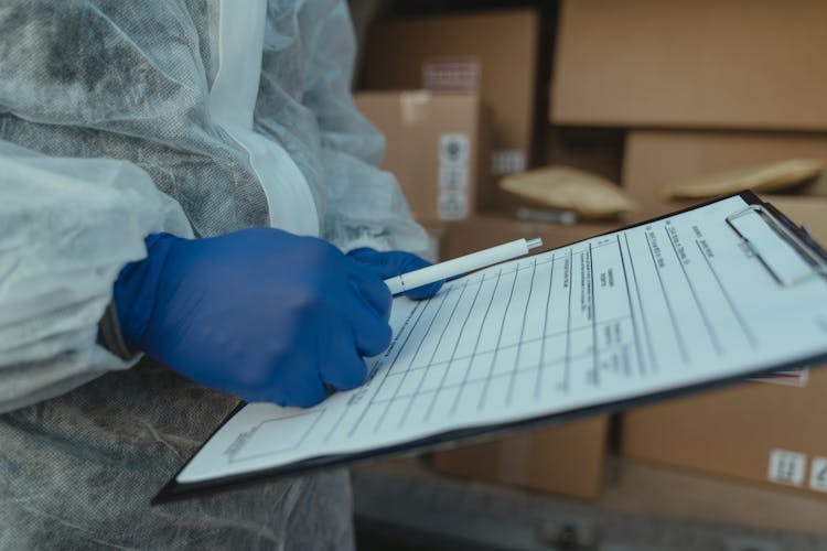 Hands Of A Person Wearing Gloves Holding A Pen And Paper On Clipboard