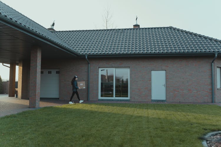 Person Holding A Box Near A Brick House