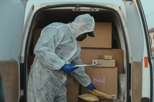 Delivery worker wearing protective gear checks and loads packages into a van.