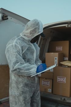 A logistics worker in PPE inspects packages in a delivery van for shipment.