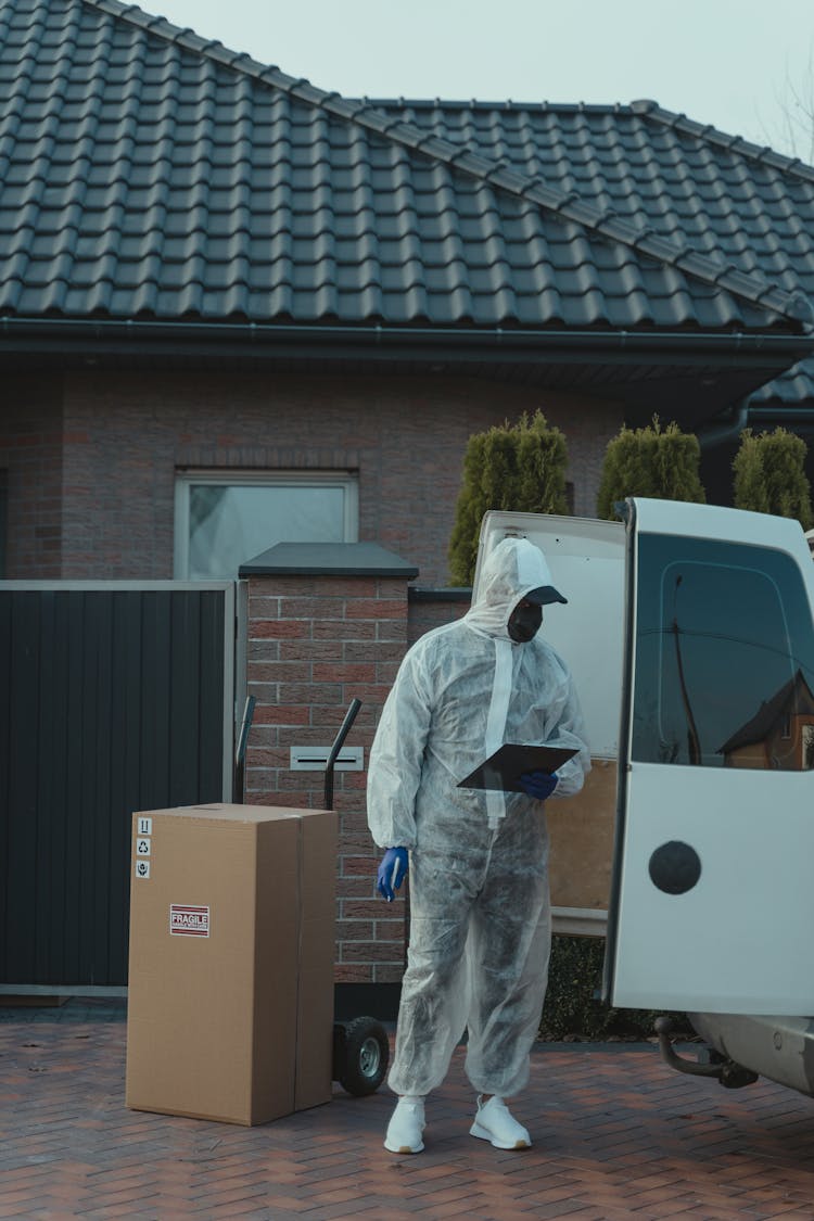 Delivery Man In PPE Standing Beside A Delivery Van 