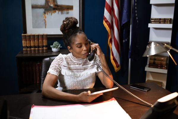 Businesswoman multitasking with phone and tablet at desk in office setting.